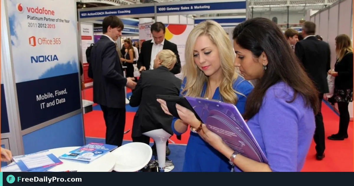Exhibitor staff capturing a booth lead on a phone while talking to a visitor at a trade show